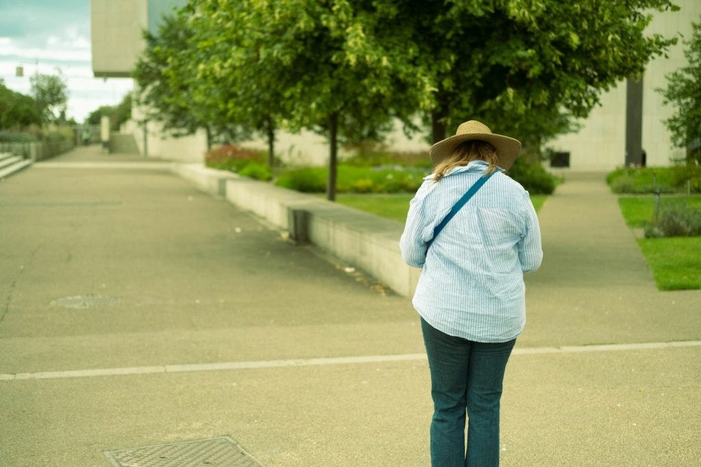 A woman wearing a hat walks along a paved outdoor path.