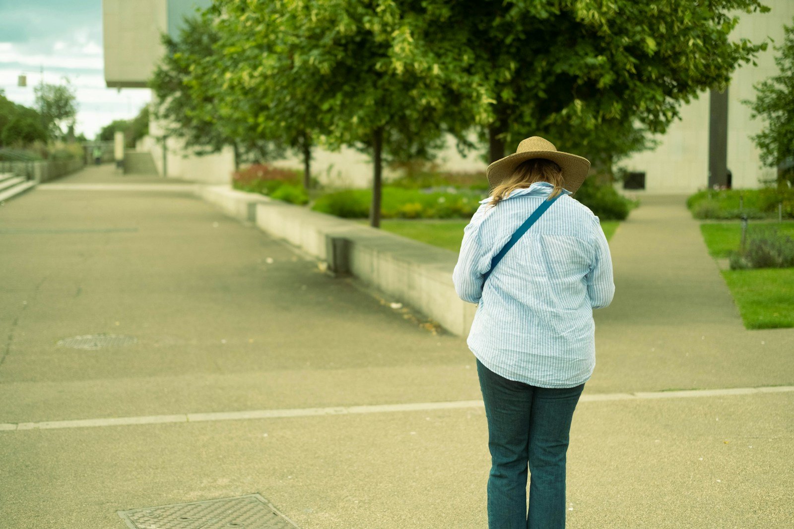 A woman wearing a hat walks along a paved outdoor path.