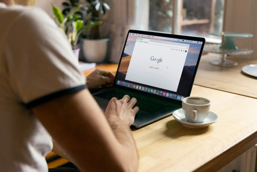 Person using a laptop showing Google Search beside a coffee cup