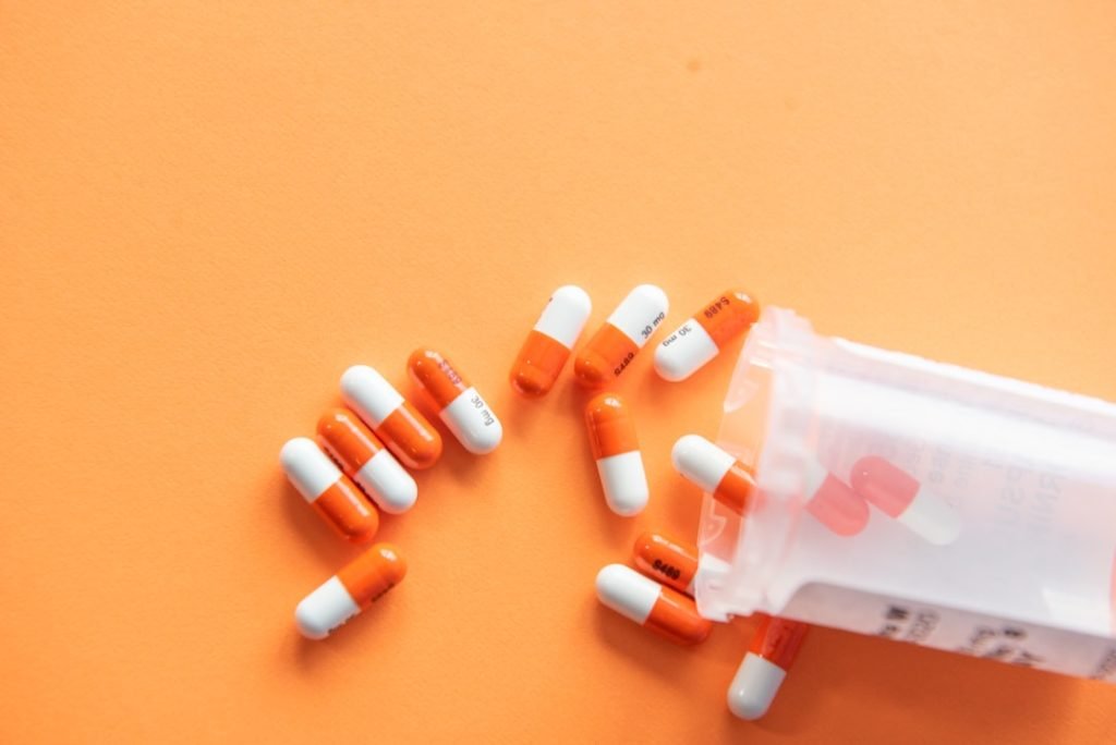 Medicine capsules beside a prescription bottle on an orange background