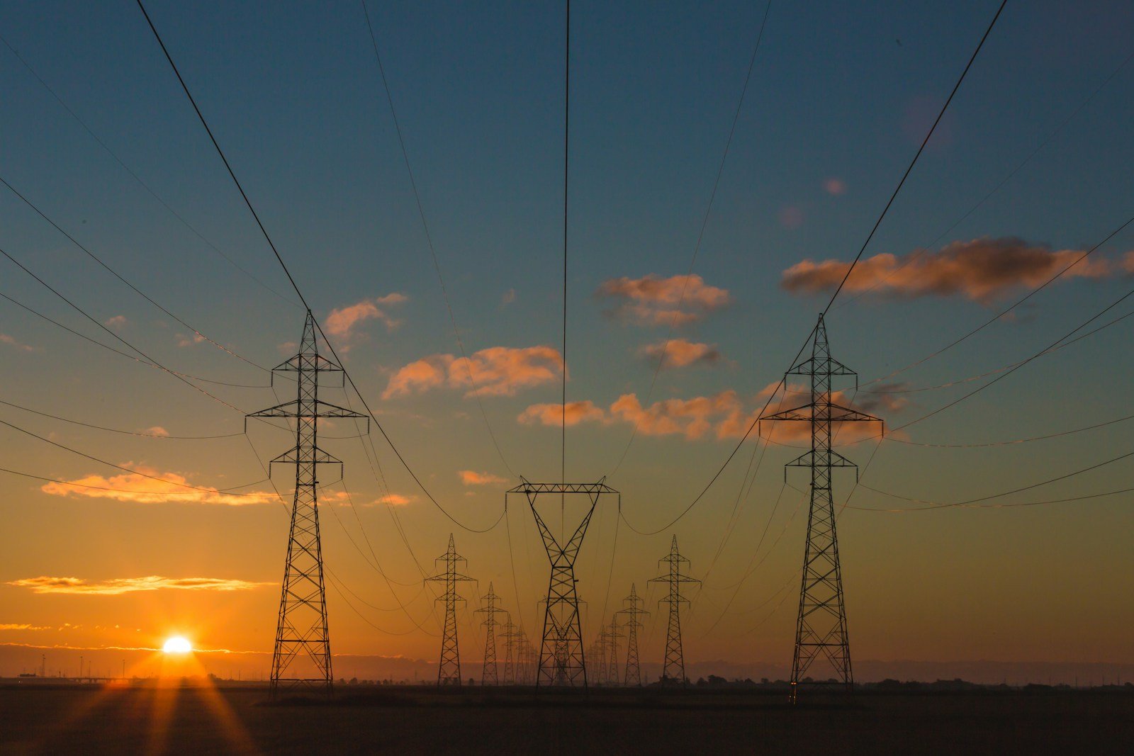 Electricity transmission towers silhouetted against the sunset.