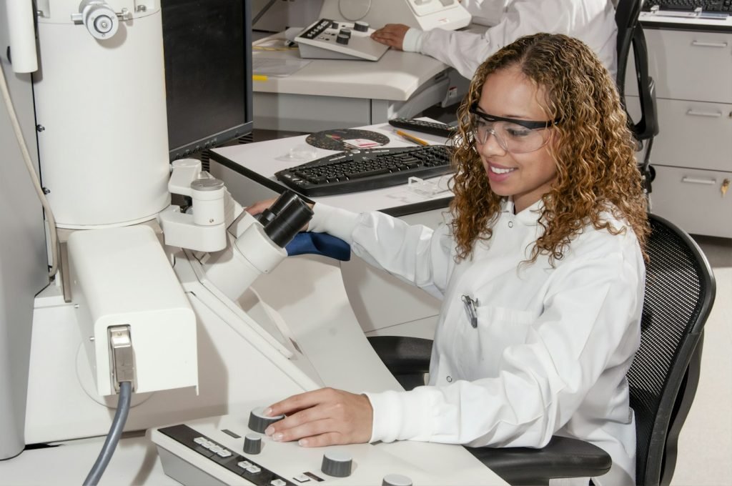 Laboratory technician operating an electron microscope beside a computer