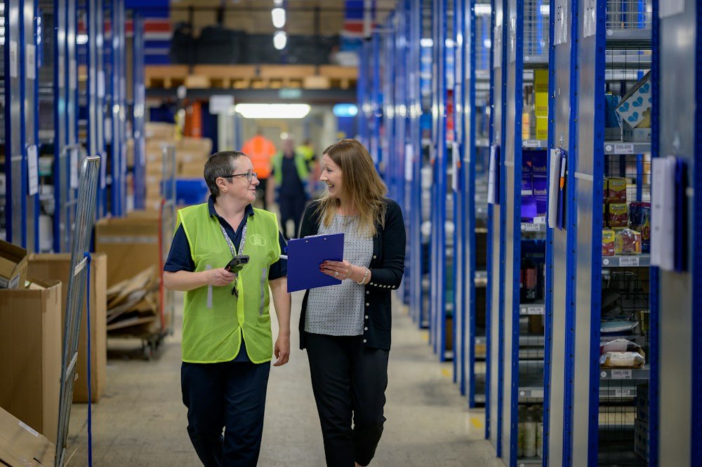 Two workers discussing a clipboard in a warehouse aisle