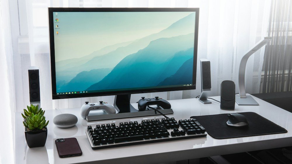 Monitor, keyboard, mouse and game controllers on a bright desk