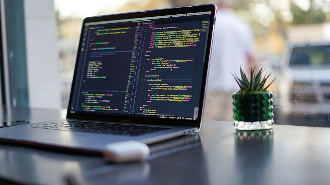 Laptop displaying programming code beside a plant